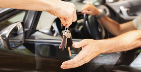 Hands of valet parking worker giving key to driver man sitting inside car. Unrecognizable man buyer taking key from brand new automobile at autosalon showroom. Car buying, renting